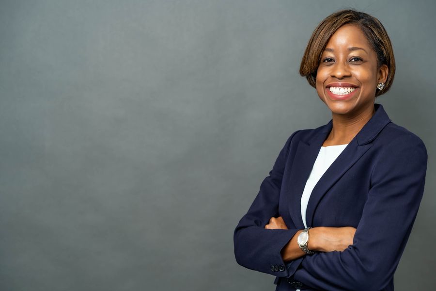 A confident Black businesswoman in a navy blazer, smiling with her arms crossed