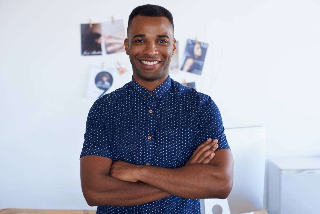 A smiling man with his arms crossed in a bright office