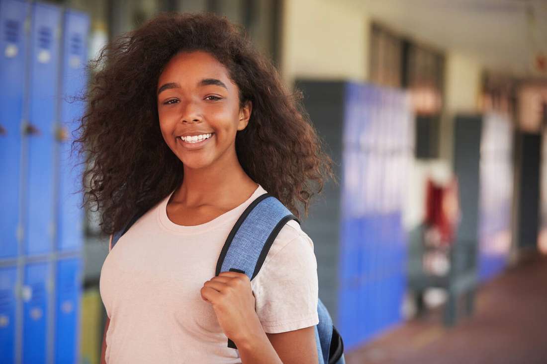 A smiling young woman with a backpack in a school hallway