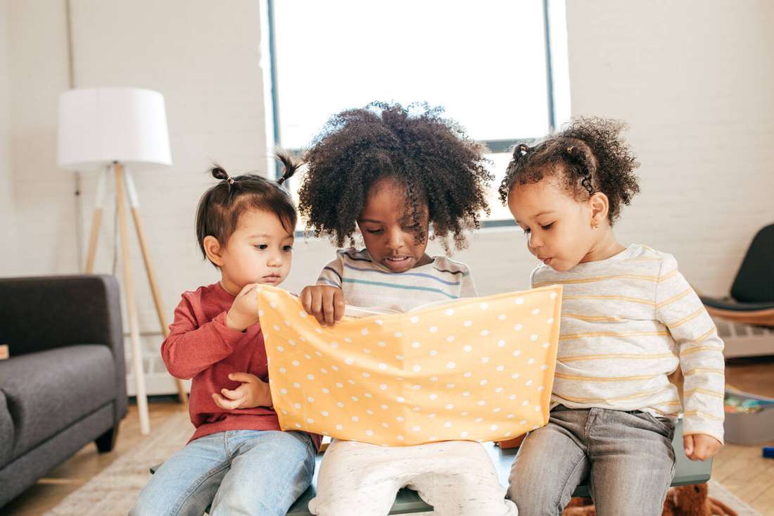 Three toddlers sharing a picture book on the floor