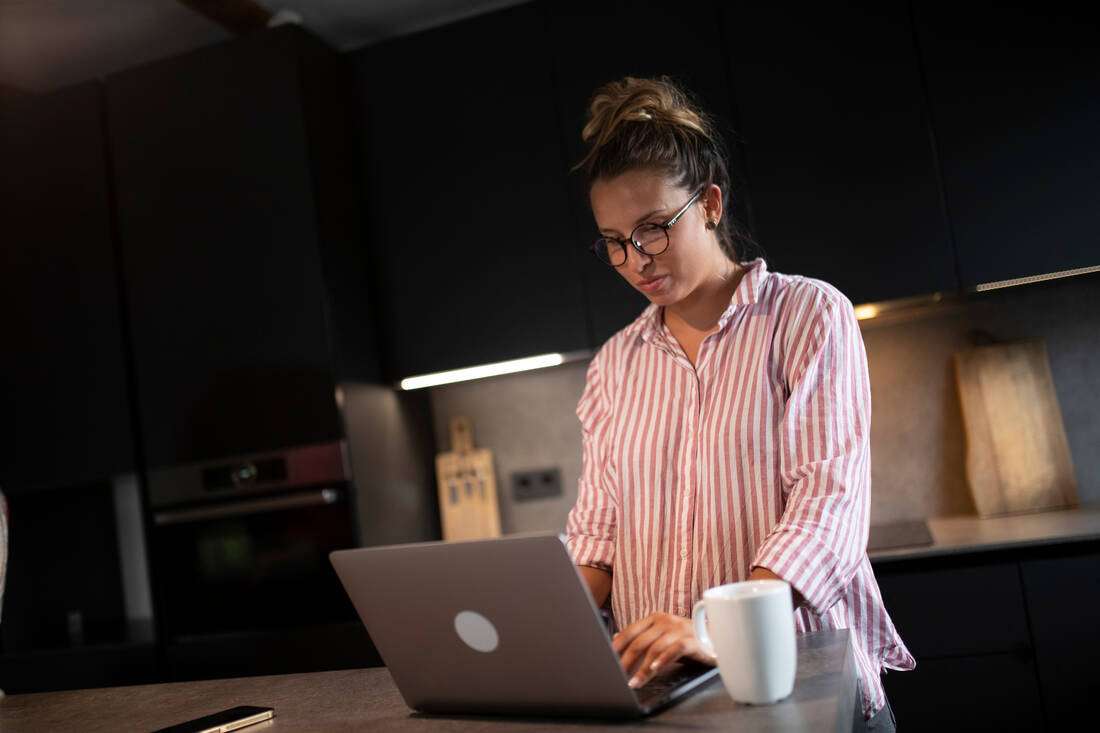 A woman working on her laptop in her kitchen with a cup of coffee